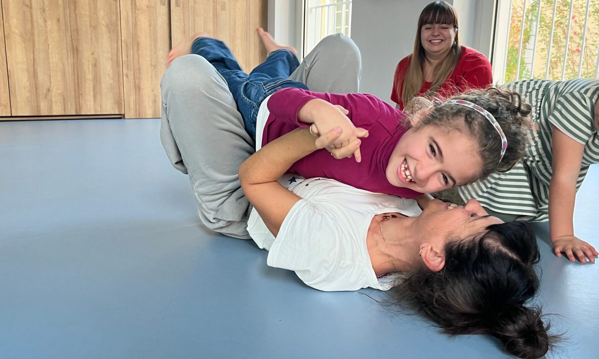 Bambina che ride mentre gioca sdraiata a terra con una donna, in un momento di affetto e divertimento durante un’attività di danza presso il Centro Paideia.