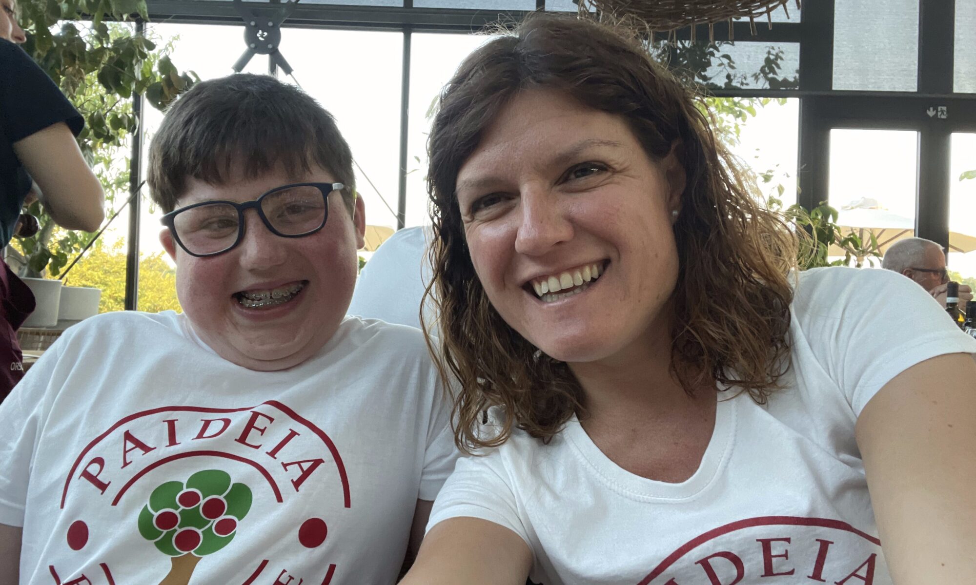 Bambino e operatrice sorridenti con maglietta della Fondazione Paideia, durante un momento conviviale.