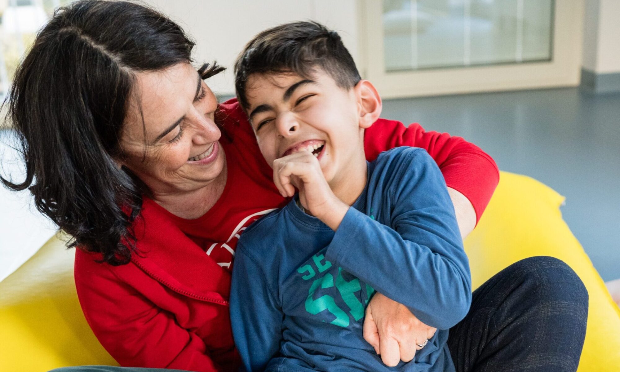 Bambino che ride in braccio a una Volontaria Paideia